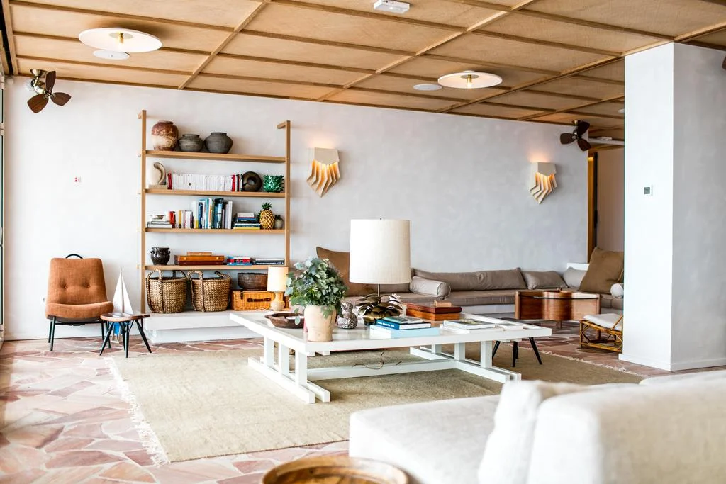 Salon moderne avec plafond en lambris de bois clair, canapé blanc, table basse, et une grande étagère décorée - Appart Hôtel Collioure - Les Suites Collection