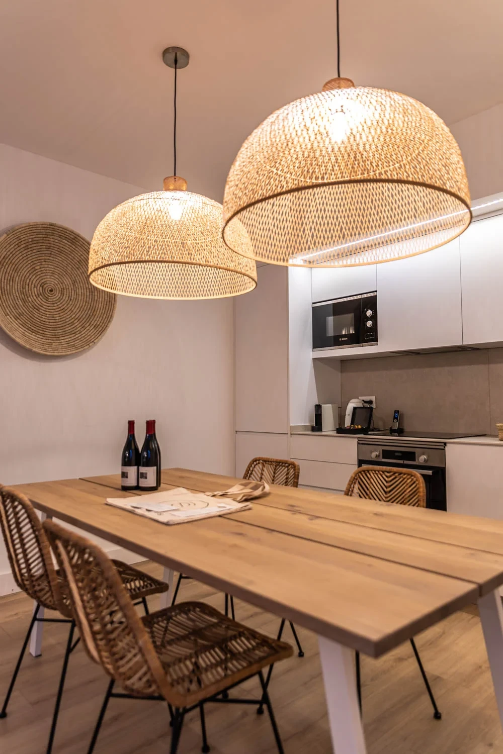 Salle à manger avec grande table en bois et suspensions lumineuses en rotin - Location Appartement Perpignan - Les Suites Collection